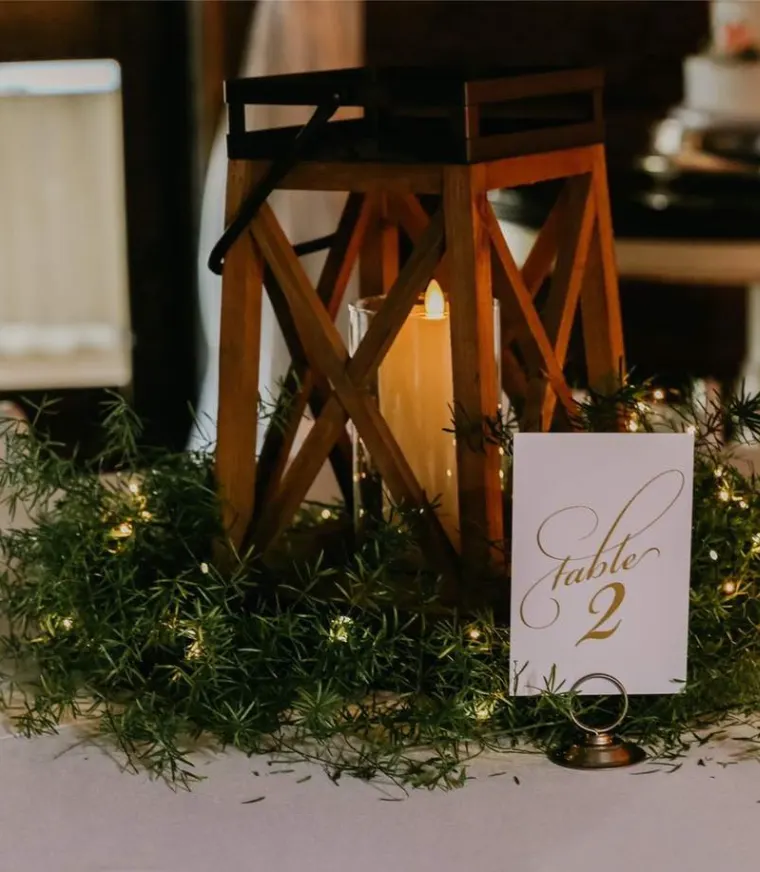 Calligraphed table number card nestled in greenery and fairy lights