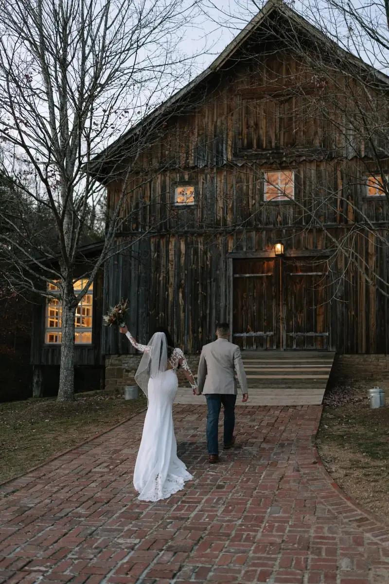Bride and groom holding hands in front of a weathered wooden barn