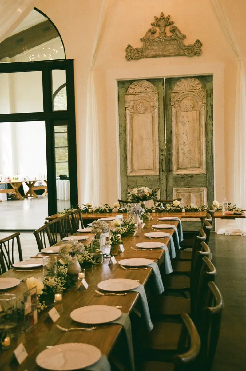 Head table set with trailing greenery and taper candles before a pair of antique doors