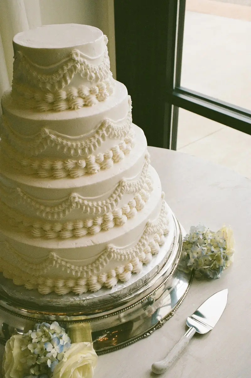 Tiered white wedding cake with piped scallop detailing and fresh blooms