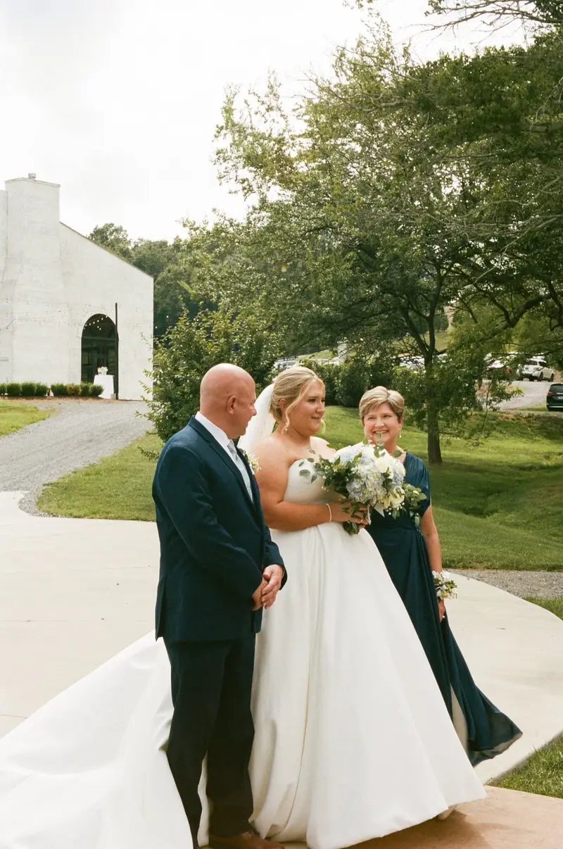 Bride standing with her parents on a lawn before the ceremony