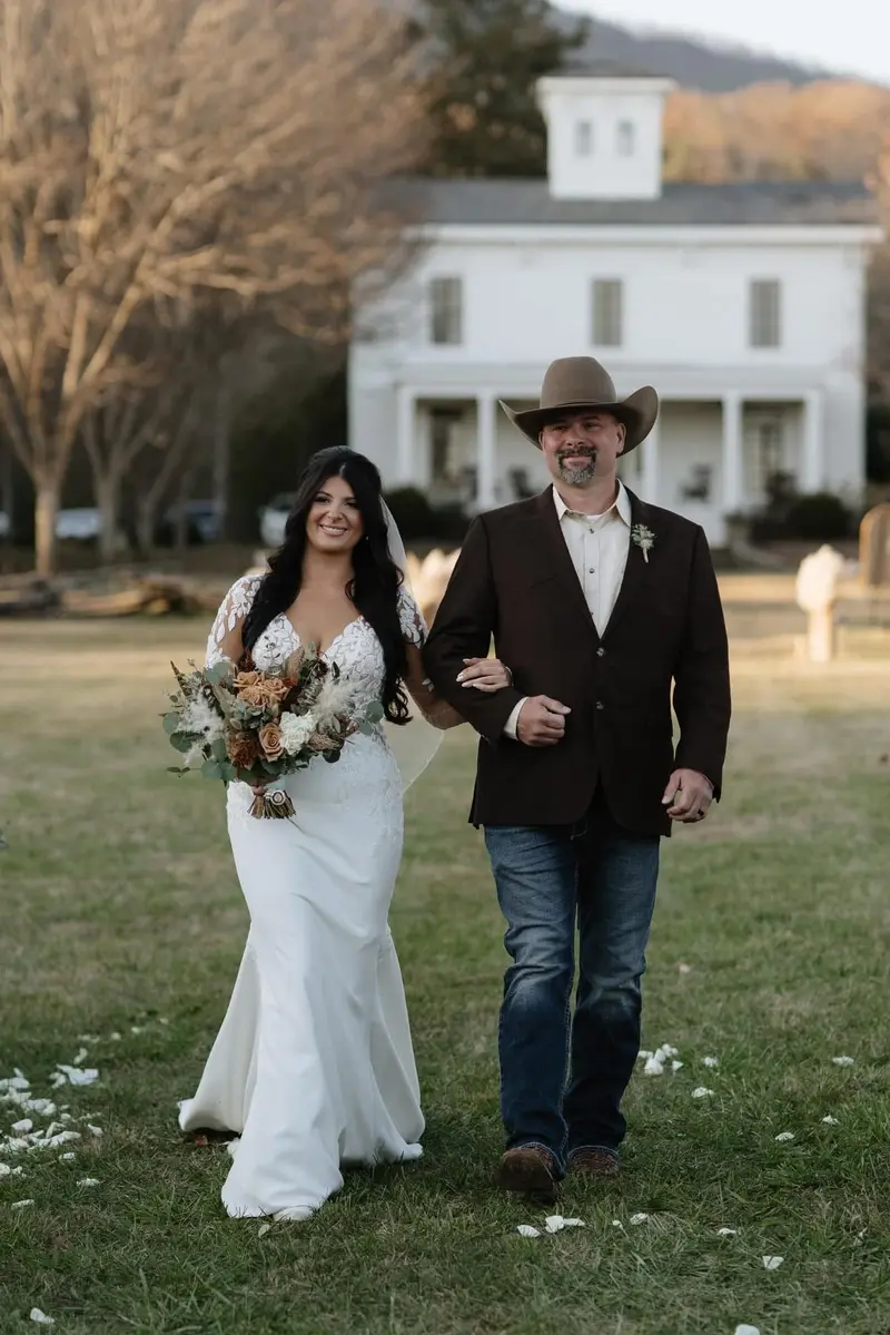 Bride walking across a lawn on her father’s arm before the ceremony