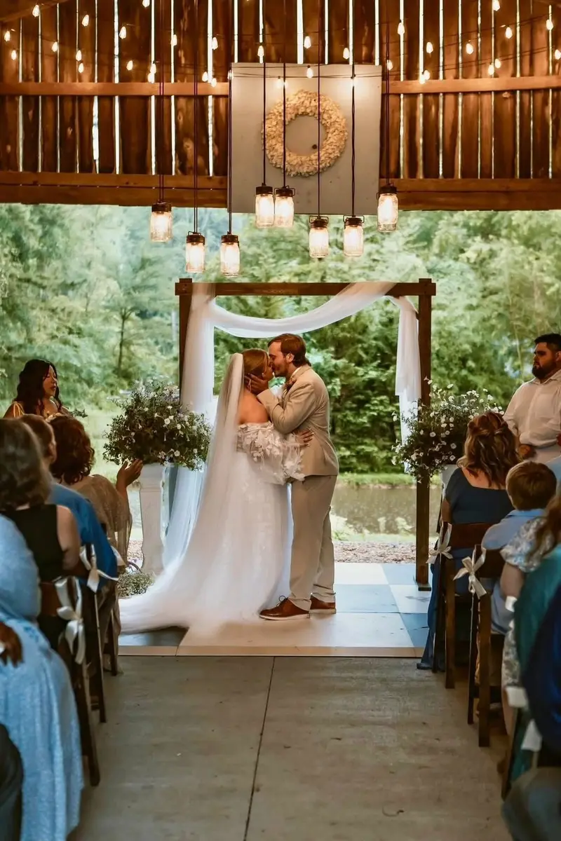 Bride and groom kissing under a draped wooden arbor during an outdoor ceremony