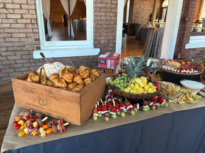 Grazing table with a crate of croissants, fresh fruit and skewers in a brick-walled venue
