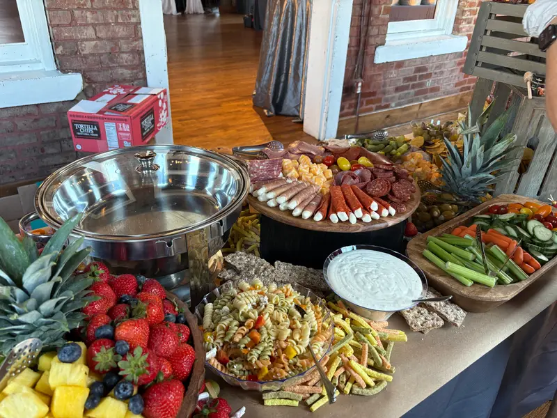 Buffet spread of strawberries, pineapple, pasta salad and crudité beside a chafing dish