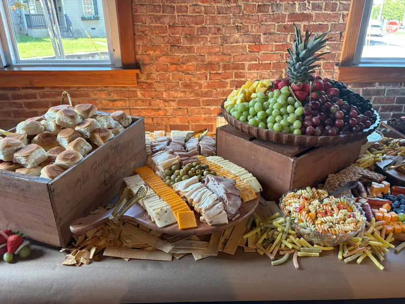 Crate of dinner rolls beside a fruit bowl topped with a pineapple and sliced cheeses