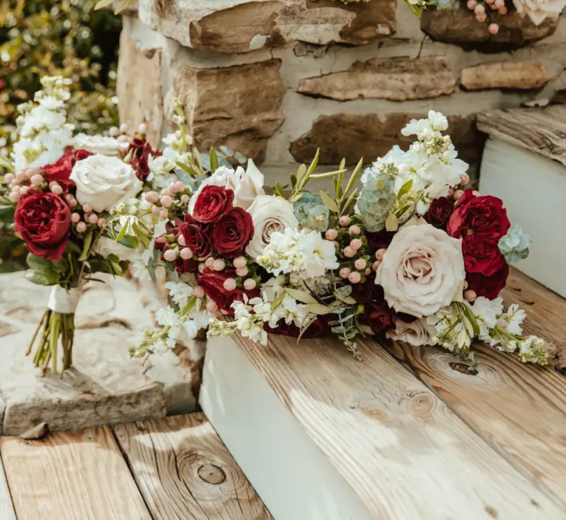 Bridal bouquets of burgundy and ivory roses resting on a wooden bench